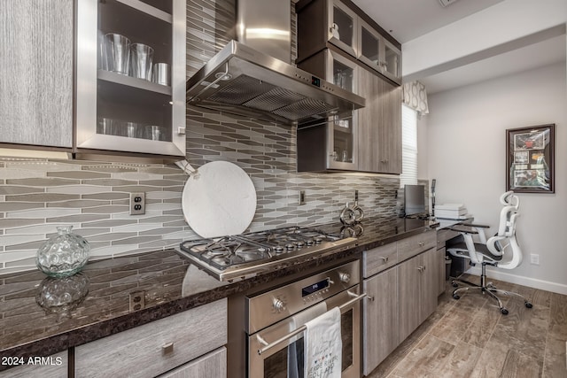 kitchen featuring light hardwood / wood-style flooring, wall chimney range hood, stainless steel appliances, dark stone countertops, and decorative backsplash