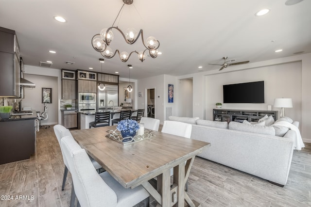 dining room with ceiling fan with notable chandelier, sink, and light hardwood / wood-style flooring