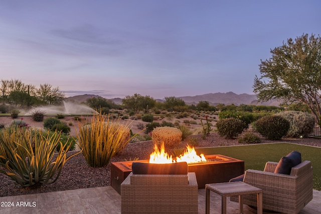 patio terrace at dusk featuring a mountain view, a fire pit, and a lawn