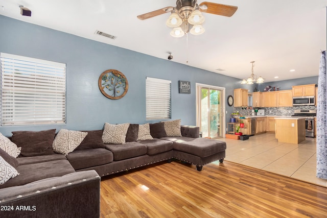 living room with ceiling fan with notable chandelier and light hardwood / wood-style flooring