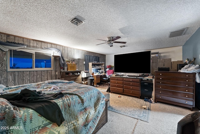 bedroom featuring ceiling fan, light colored carpet, a textured ceiling, and wooden walls