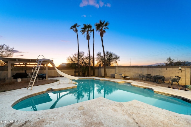 pool at dusk with a patio area and a water slide