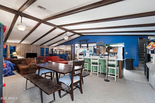 dining space with bar, lofted ceiling with beams, light carpet, and a textured ceiling