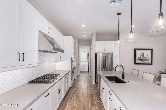 kitchen featuring tasteful backsplash, white cabinets, stainless steel appliances, sink, and hanging light fixtures