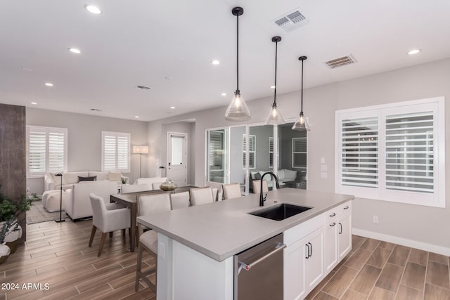 kitchen featuring a kitchen island with sink, pendant lighting, sink, stainless steel dishwasher, and white cabinetry