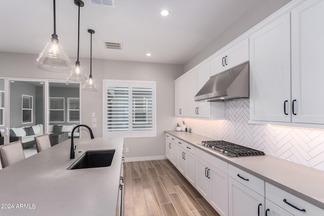 kitchen featuring pendant lighting, white cabinetry, backsplash, light wood-type flooring, and sink