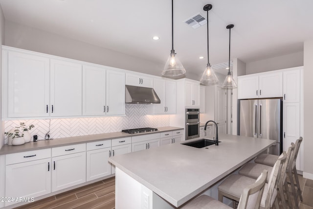 kitchen with an island with sink, decorative light fixtures, white cabinets, backsplash, and sink