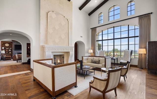 sitting room with a lit fireplace, a high ceiling, hardwood / wood-style floors, and beamed ceiling