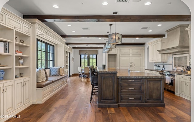 kitchen with dark wood finished floors, stainless steel range, custom range hood, visible vents, and dark stone countertops