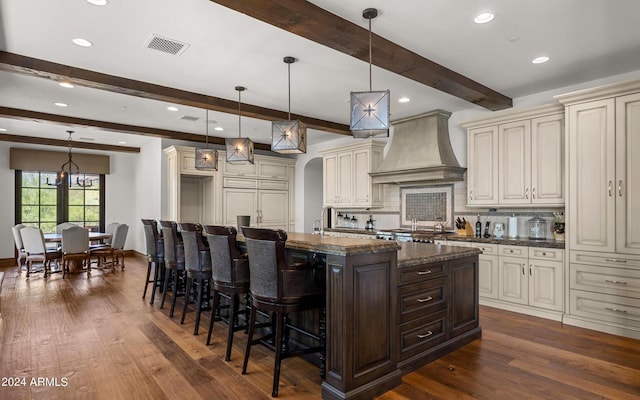 kitchen with cream cabinetry, visible vents, an island with sink, and custom exhaust hood