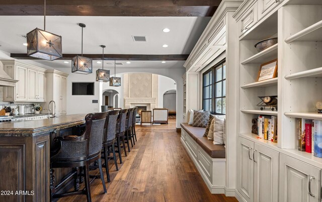 kitchen featuring arched walkways, a breakfast bar area, visible vents, beamed ceiling, and dark wood finished floors