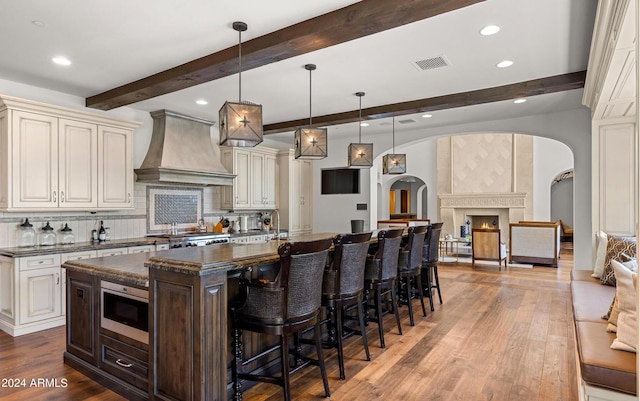 kitchen with arched walkways, a spacious island, stainless steel microwave, premium range hood, and a kitchen breakfast bar