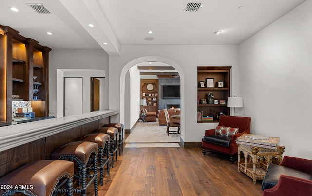 bar featuring built in shelves, visible vents, a fireplace, and wood finished floors