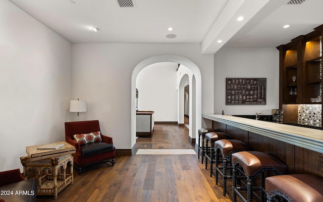 bar with arched walkways, decorative backsplash, wood-type flooring, indoor wet bar, and recessed lighting