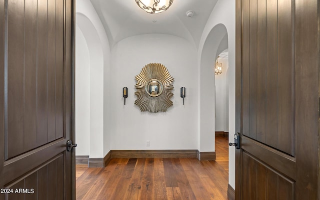 corridor with lofted ceiling, arched walkways, hardwood / wood-style flooring, and baseboards