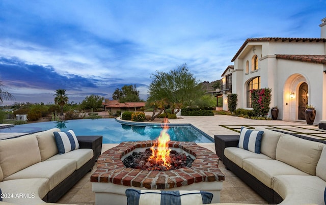 pool at dusk with a patio area, an infinity pool, and an outdoor hangout area