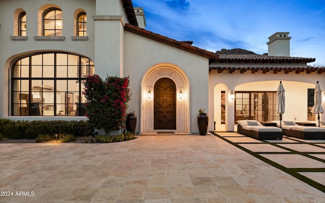 entrance to property featuring a patio area, a tile roof, a chimney, and stucco siding