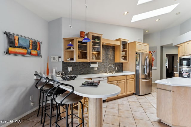 kitchen with stainless steel appliances, a peninsula, a skylight, a sink, and light brown cabinetry