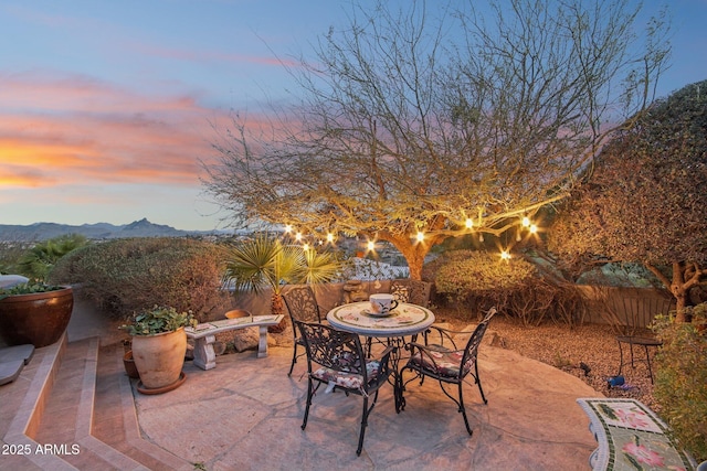 patio terrace at dusk featuring outdoor dining space, fence, and a mountain view