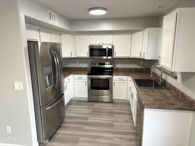 8514 S 49th Dr, Laveen, AZ 85339 - kitchen featuring stainless steel appliances, a sink, dark countertops, white cabinetry, and light wood-style flooring