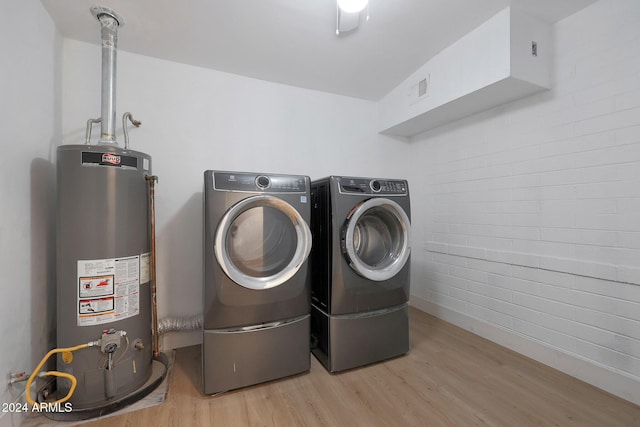 washroom featuring brick wall, light hardwood / wood-style floors, gas water heater, and independent washer and dryer