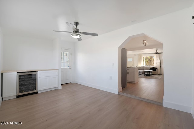 unfurnished living room featuring light wood-type flooring, wine cooler, and ceiling fan