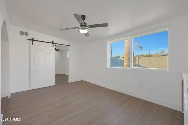 unfurnished bedroom featuring a barn door, light hardwood / wood-style flooring, and ceiling fan