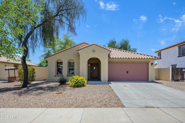 mediterranean / spanish house featuring fence, an attached garage, a tile roof, stucco siding, and concrete driveway