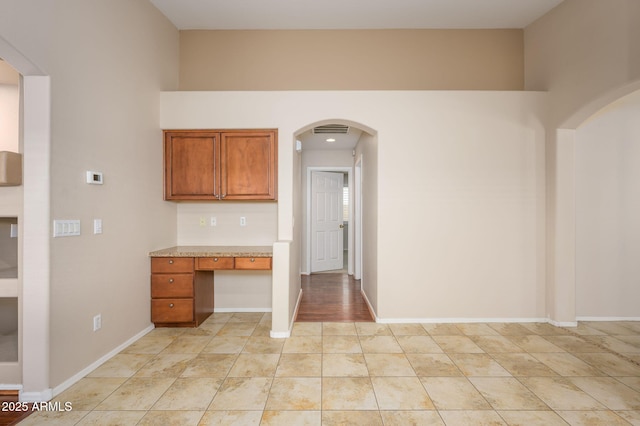 kitchen with brown cabinetry, visible vents, built in study area, light tile patterned floors, and baseboards