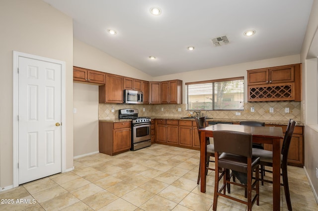 kitchen with appliances with stainless steel finishes, tasteful backsplash, brown cabinets, and visible vents