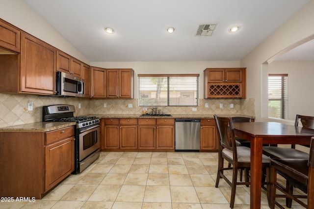 kitchen featuring brown cabinets, a sink, stainless steel appliances, a wealth of natural light, and visible vents