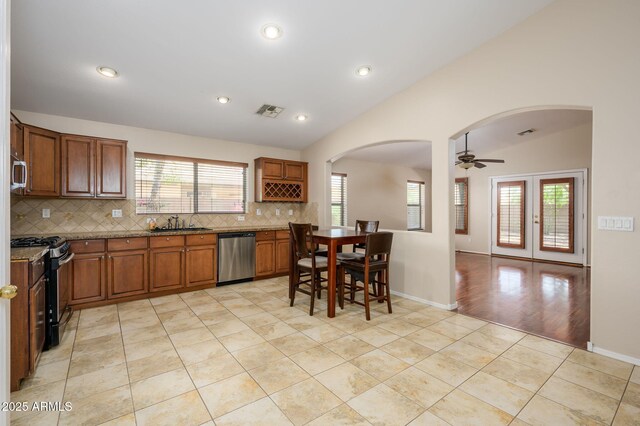 kitchen featuring a sink, arched walkways, stainless steel appliances, tasteful backsplash, and vaulted ceiling