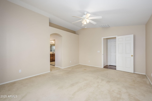 spare room with carpet floors, lofted ceiling, baseboards, arched walkways, and a ceiling fan