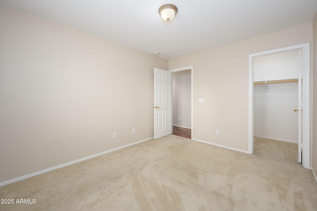 unfurnished bedroom featuring baseboards, light colored carpet, a walk in closet, and a closet