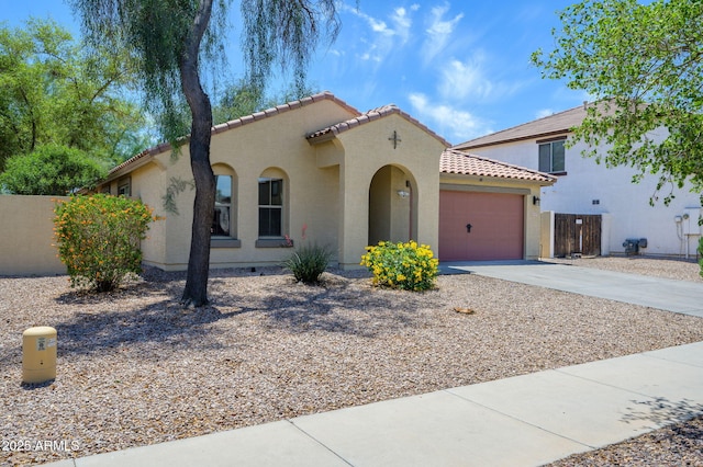 mediterranean / spanish home featuring fence, an attached garage, stucco siding, concrete driveway, and a tiled roof