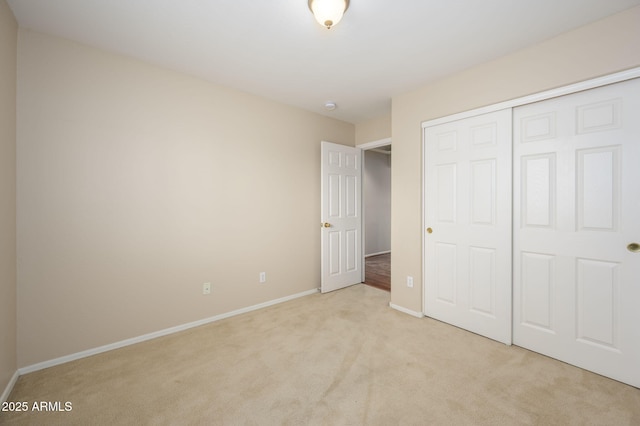 unfurnished bedroom with baseboards, a closet, and light carpet