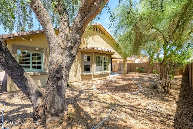 rear view of house featuring a fenced backyard, stucco siding, and a tiled roof