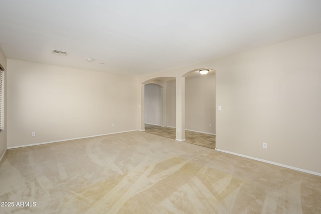 empty room featuring visible vents, arched walkways, baseboards, and light carpet
