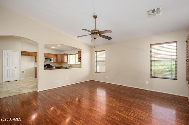 unfurnished living room with a ceiling fan, arched walkways, visible vents, and light wood-type flooring