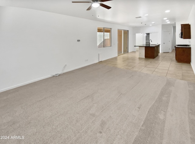 unfurnished living room with ceiling fan, sink, and light carpet