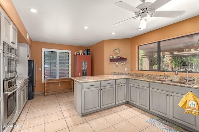 kitchen with a sink, a peninsula, light tile patterned flooring, and oven