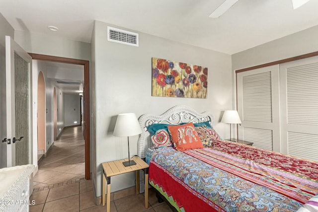 tiled bedroom with visible vents, arched walkways, a closet, and a ceiling fan