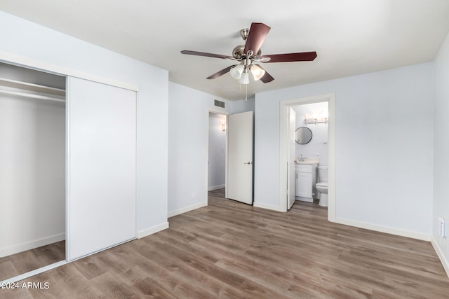 unfurnished bedroom with wood-type flooring, a closet, ensuite bath, and ceiling fan