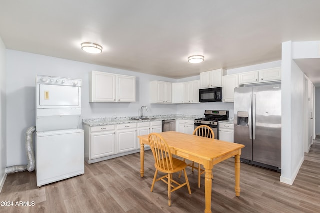 kitchen featuring sink, white cabinetry, appliances with stainless steel finishes, light wood-type flooring, and stacked washer and dryer