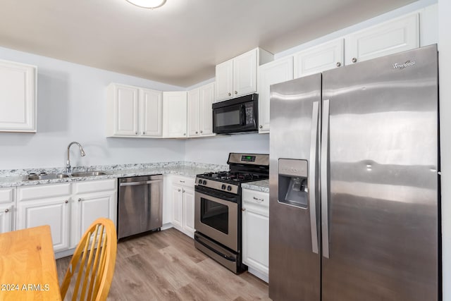 kitchen featuring appliances with stainless steel finishes, white cabinetry, light stone countertops, light hardwood / wood-style flooring, and sink