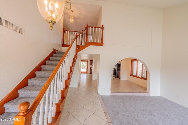 stairway with carpet floors, arched walkways, visible vents, a high ceiling, and tile patterned flooring