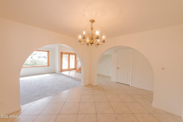 empty room featuring arched walkways, light carpet, a notable chandelier, and light tile patterned floors