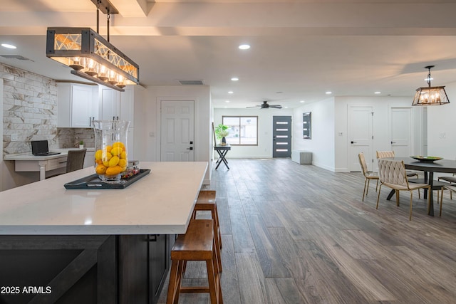 kitchen featuring white cabinets, a center island, decorative backsplash, hardwood / wood-style flooring, and a breakfast bar area