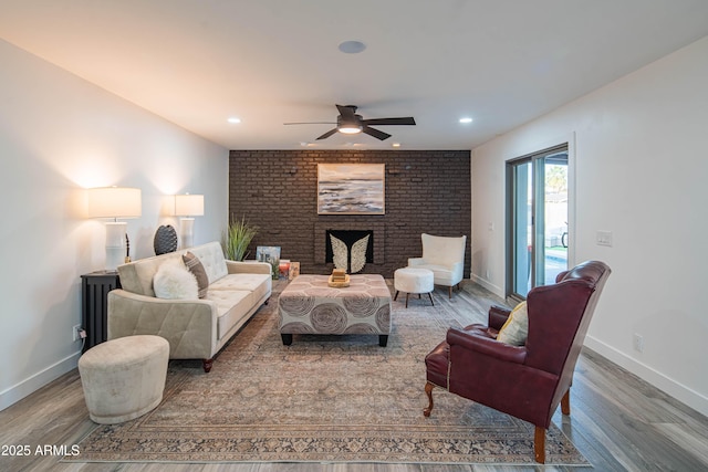 living room featuring ceiling fan, hardwood / wood-style flooring, brick wall, and a brick fireplace