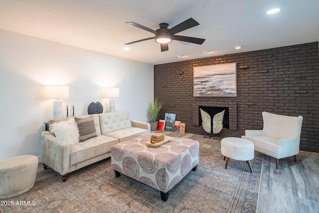 living room with ceiling fan, brick wall, hardwood / wood-style floors, and a fireplace